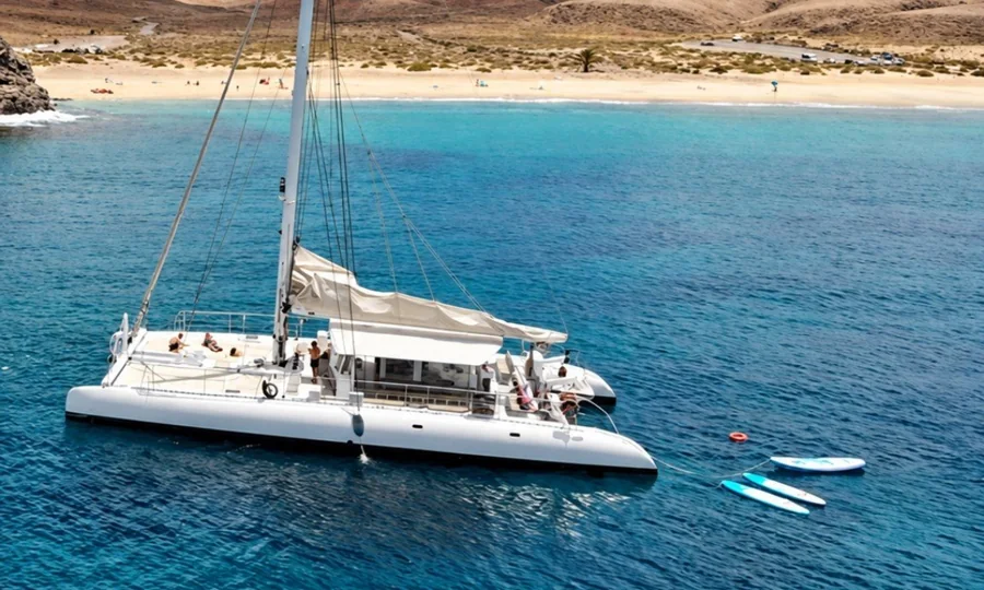 Golden Lanzarote beach and turquoise water with a white catamaran anchored offshore