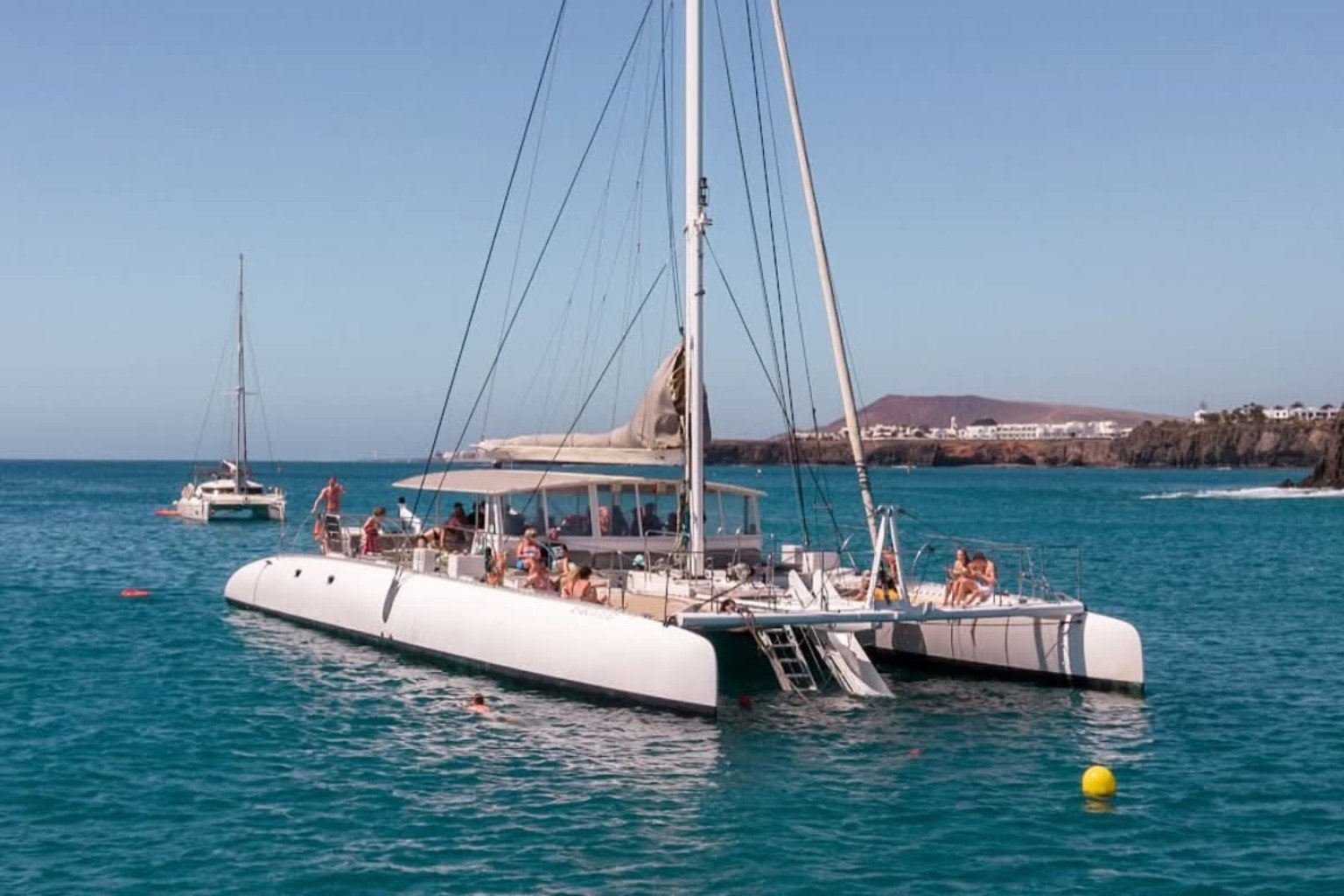 Guests relaxing aboard Papagayo Sail catamaran on turquoise water off Lanzarote